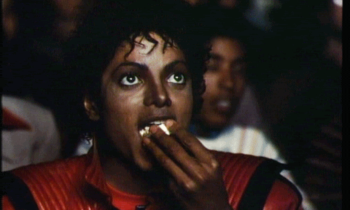 GiIF do cantor Michael Jackson comendo pipoca e sorrindo dentro de um cinema