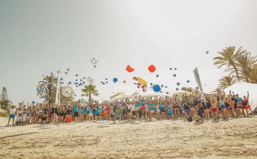 Vários participantes do SEOnthebeach na praia, na areia, em diversas poses, levantando os braços, sorrindo, jogando balões para o alto